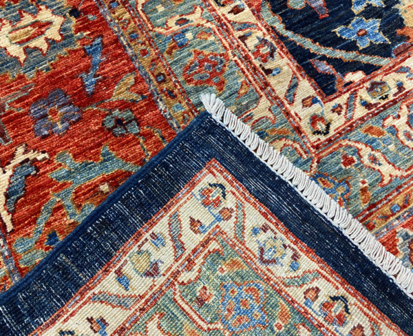 Bold large rug with navy and rust tones and a red and gold border. This area rug is hand-knotted with wool.