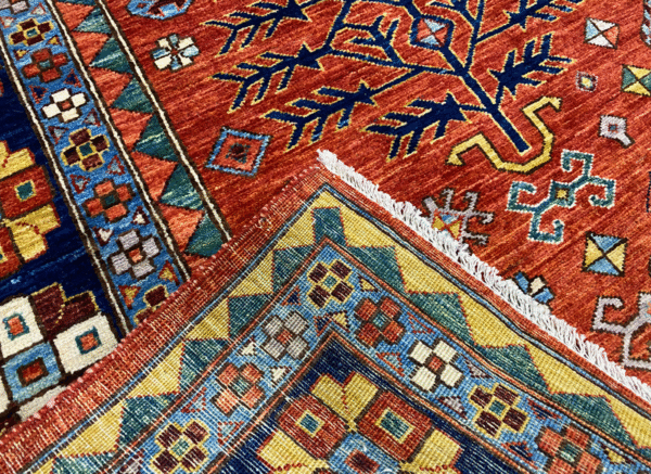 Bold large rug with deep red/rust tones and a blue border. This area rug is hand-knotted with wool.