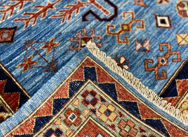 This bold tribal area rug is 6x9 featuring a blue background with tribal geometric shapes with a tribal styled border and short fringe.