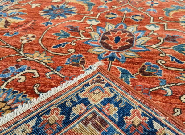 Bold large rug with deep rust tones and a blue border with yellow designs. This area rug is hand-knotted with wool.