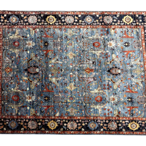 Large 9x12 tribal area rug with a blue background and ivory and rust tribal designs with a large border. This area rug is hand-knotted with wool.